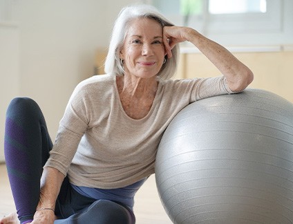Senior woman smiling while resting against balance ball