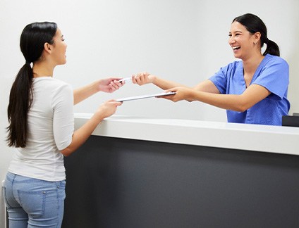 Smiling dental assistant handing patient form